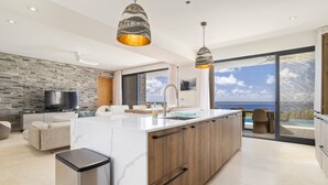 Una cocina moderna con una isla grande, una pared de piedra, un televisor de pantalla plana y vistas al océano.
