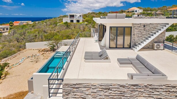 Una villa moderna con piscina, mobiliario exterior y vistas al mar.