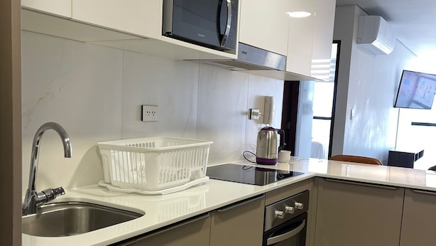 Una cocina moderna con un lavaplatos de acero inoxidable, un microondas y una tetera.