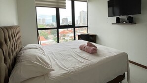 Un dormitorio con cama, televisor montado en la pared y ventana con persianas.
