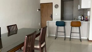 Un comedor con una mesa de vidrio y sillas de madera, una cocina con armarios blancos y una puerta que da a otra habitación.