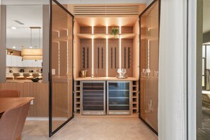 Eine moderne Küche mit Holzausbau, ein Essbereich mit Tisch und Stühlen sowie eine integrierte Weinkühlbox mit Gläsern.