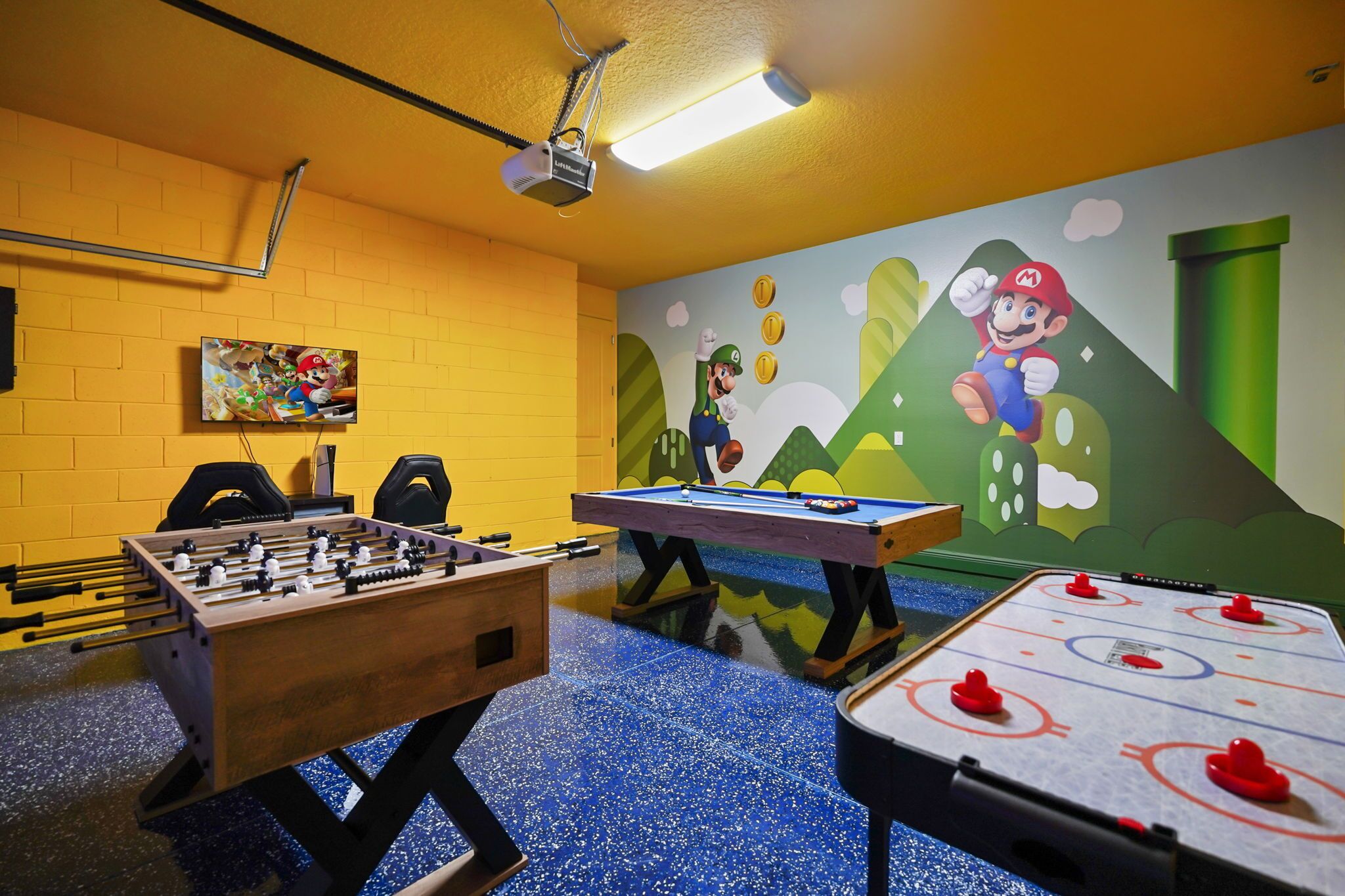 A room with a foosball table, a pool table, and a Mario-themed mural.