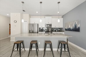 Eine moderne Küche mit einer zentralen Kochinsel, Edelstahlgeräten, Pendelleuchten und einem großen Gemälde an der Wand.