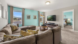Een woonkamer met een grote flatscreen televisie, een zithoek, een salontafel en een lamp.