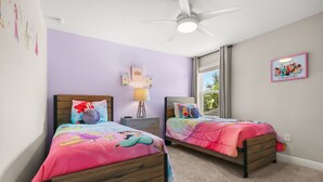 Een slaapkamer met twee bedden, een plafondventilator en een raam met gordijnen.