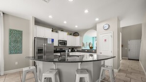 Een moderne keuken met witte kasten, een centraal eiland met barkrukken, een magnetron en een roestvrijstalen koelkast.