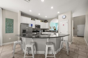 A modern kitchen with white cabinets, a central island with stools, a microwave, and a stainless steel refrigerator. - The Ultimate Private Oasis & Game Room 6 BD/ 3.5 BA/ Solterra Resort (5140 OA) (Davenport)