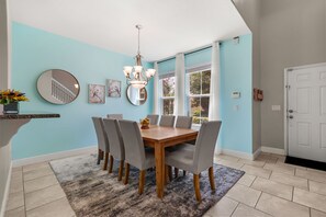 A dining area with a wooden table, grey upholstered chairs, a fluffy rug, and a chandelier. - The Ultimate Private Oasis & Game Room 6 BD/ 3.5 BA/ Solterra Resort (5140 OA) (Davenport)