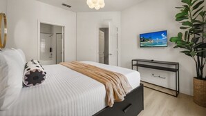 Quarto com cama, mesa de cabeceira, televisão e uma planta grande.
