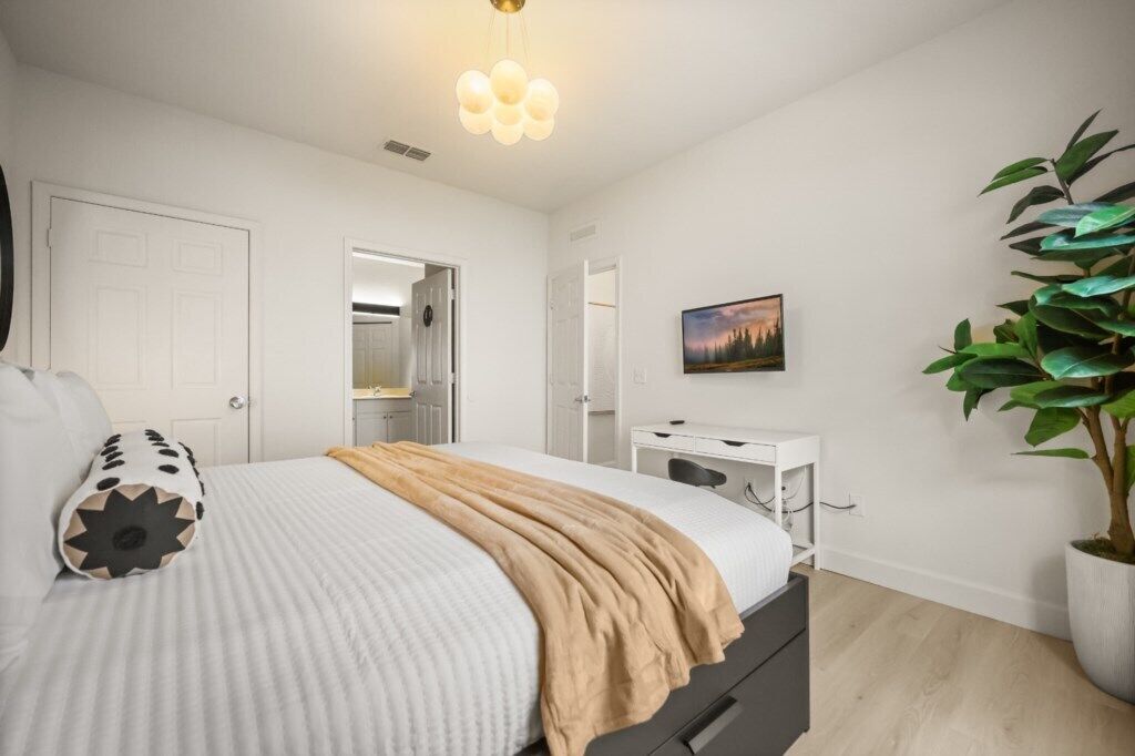 Un dormitorio con cama, mesita de noche, cómoda y planta en maceta.