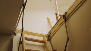 Una escalera de madera con barandillas de metal, una lámpara en el techo y una puerta al final.