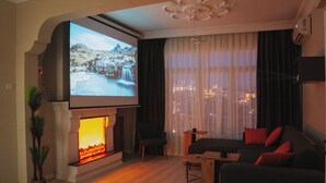 Una sala de estar con chimenea, una pantalla grande, un sofá y vistas de la ciudad de noche.