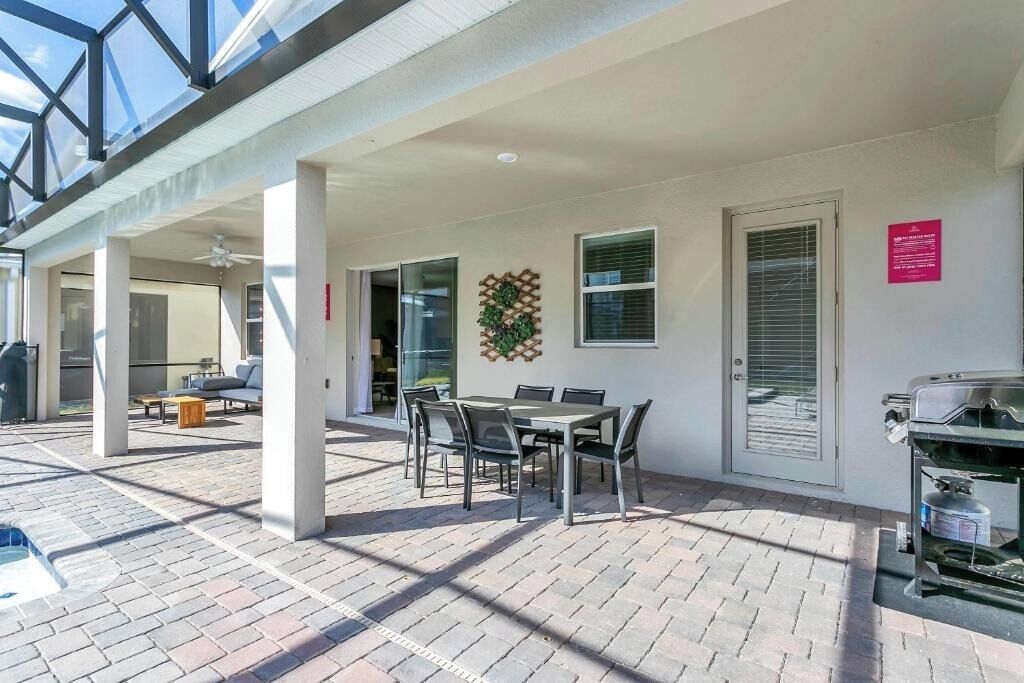 A covered outdoor patio with a table and chairs, a grill, and a view of the sky.
