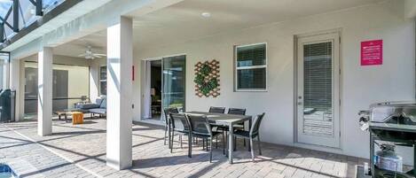 A covered outdoor patio with a table and chairs, a grill, and a view of the sky.