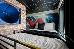 Ein modernes Schlafzimmer mit Ziegelwand, einem großen Bett mit weißer und schwarzer Bettwäsche, einem Wandgemälde zum Thema Spider-Man und einer blauen Rutsche.