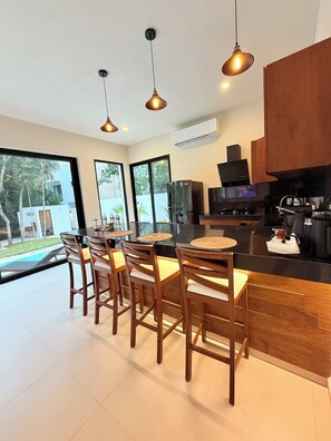 A modern kitchen with a central island, bar stools, pendant lighting, and a view of the outdoors. - Your luxury hideaway with private pool and perfect location in Riviera Maya (Puerto Morelos)