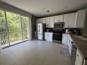 A modern kitchen with white cabinets, stainless steel appliances, and a large sliding glass door to a balcony. - 3 BD/ 3.5  BA/ Vista Cay (5076-90 TC) (Orlando)