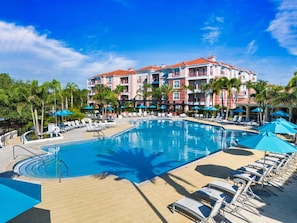 A large swimming pool surrounded by lounge chairs and umbrellas, with a multi-story building in the background. - Vista Cay Retreat: Stunning 3-Level Townhome/ 3 BD/ 3.5  BA (5076-90 TC) (Orlando)