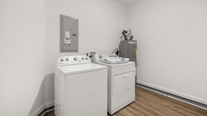 Ein Waschraum mit Waschmaschine und Trockner, einem Stromzähler und einem Warmwasserbereiter.
