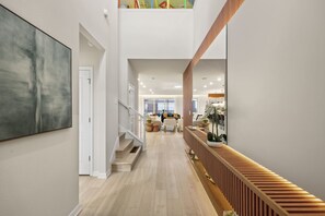 A spacious interior with a staircase leading to a second floor, a large abstract painting on the left, and a wooden bench with potted plants on the right. - 8 BD/ 6 BA/ Windsor Cay (1025 BW) (Clermont)