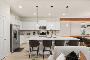 A modern kitchen with white cabinets, a stainless steel refrigerator, a central island with bar stools, and pendant lighting. - 8 BD/ 6 BA/ Windsor Cay (1025 BW) (Clermont)