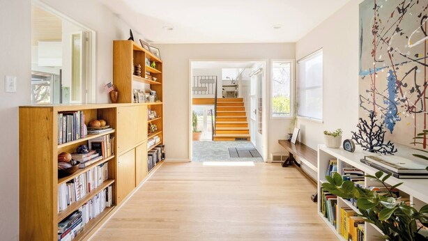 A spacious hallway with wooden bookshelves, a staircase, and a large abstract painting. - An updated mid-century modern house in one of Boulder's best neighborhoods. (Boulder)