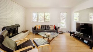 A living room with a fireplace, a black leather sofa, a glass coffee table, and a TV. - An updated mid-century modern house in one of Boulder's best neighborhoods. (Boulder)