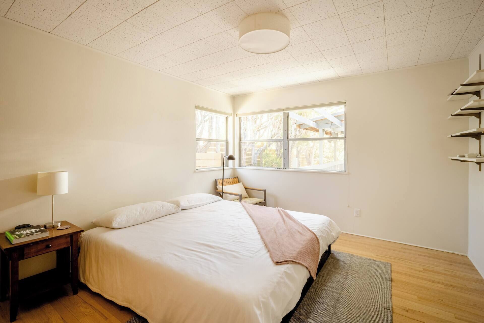 A bedroom with a bed, bedside table, lamp, and a window with a view.
