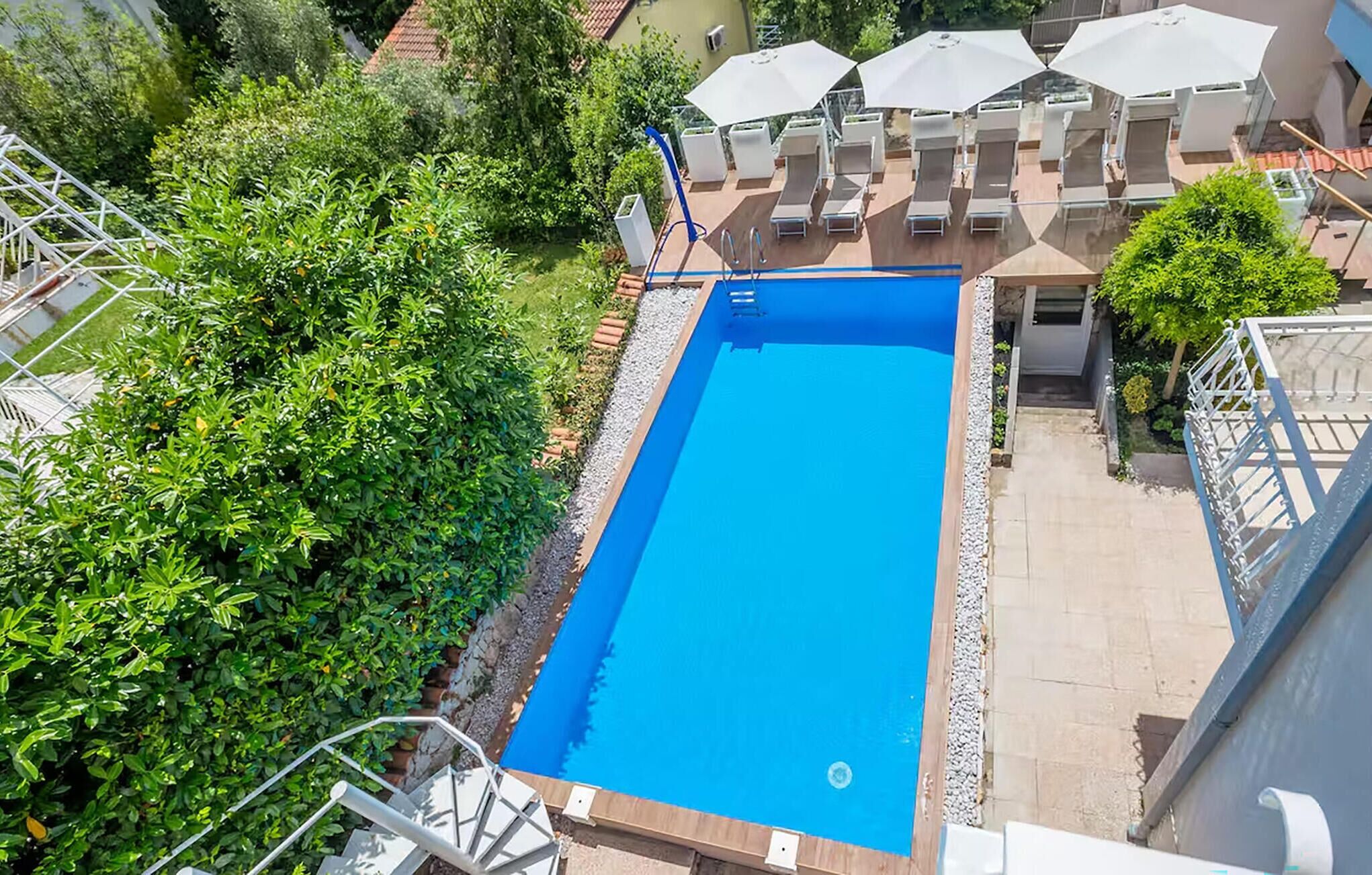 A rectangular swimming pool with a blue interior, surrounded by a white pool deck and a metal safety railing.