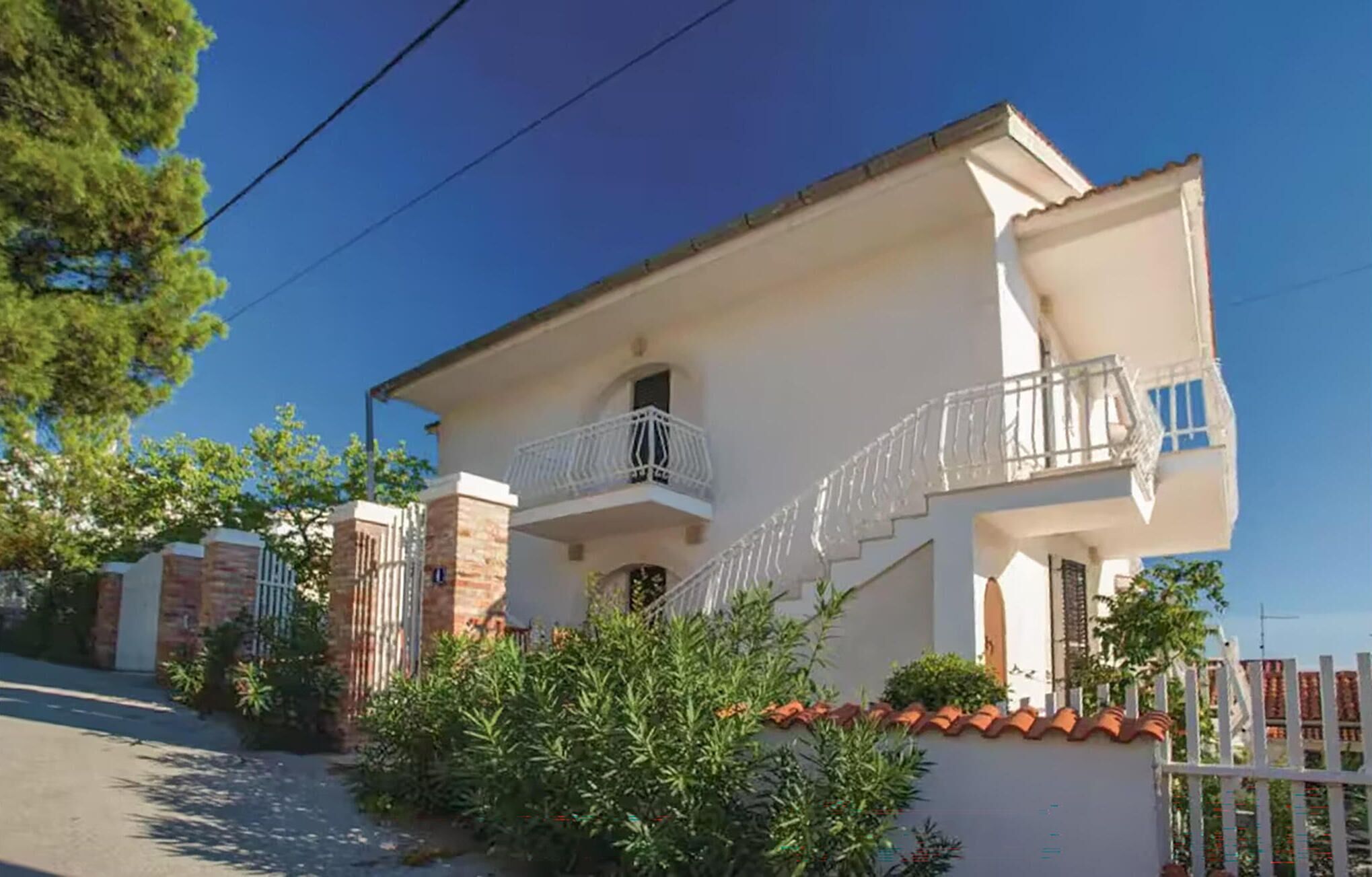 A two-story house with a balcony, a gated entrance, and a small garden.