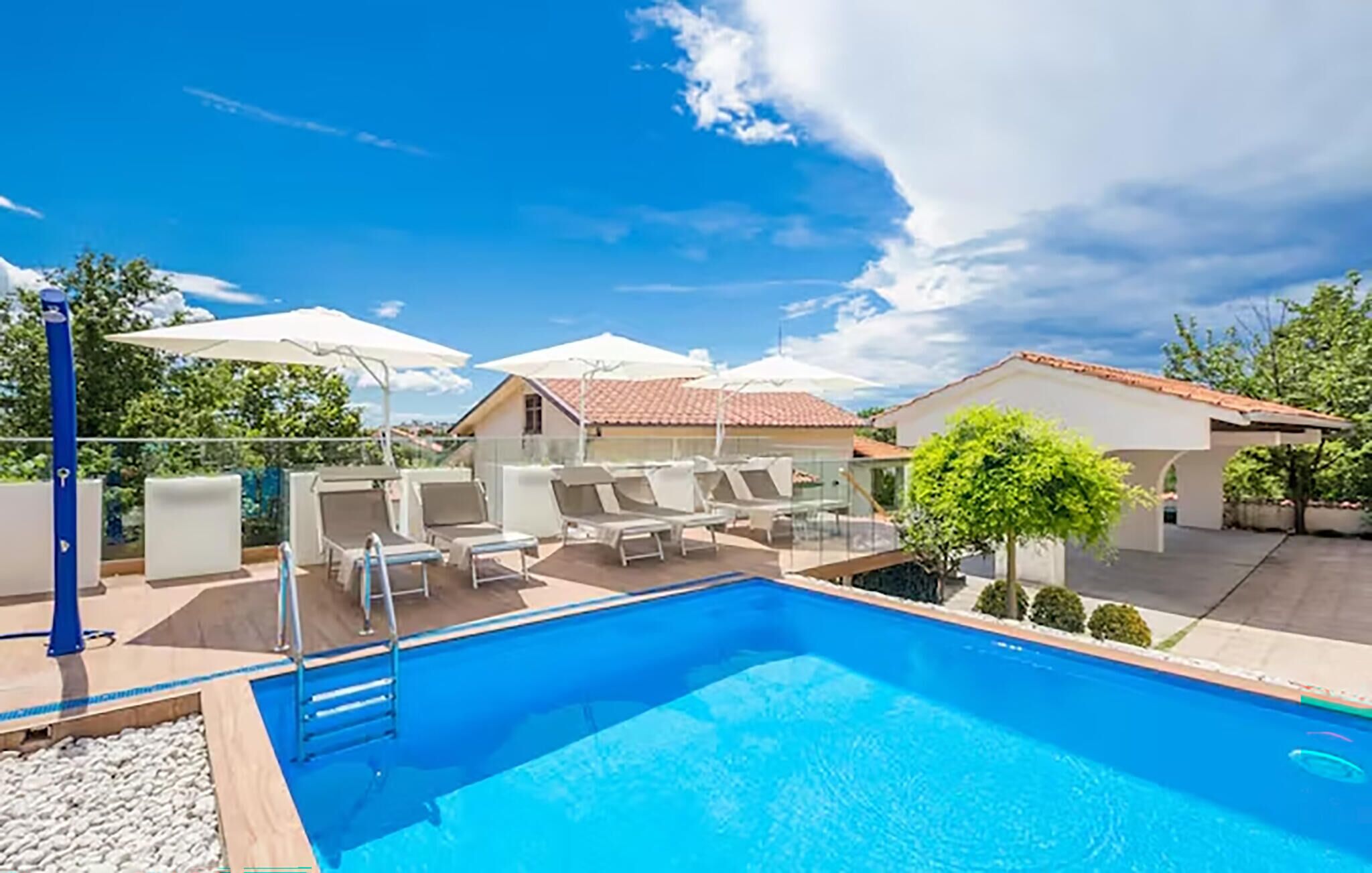 A swimming pool with lounge chairs and umbrellas, surrounded by buildings with red-tiled roofs.