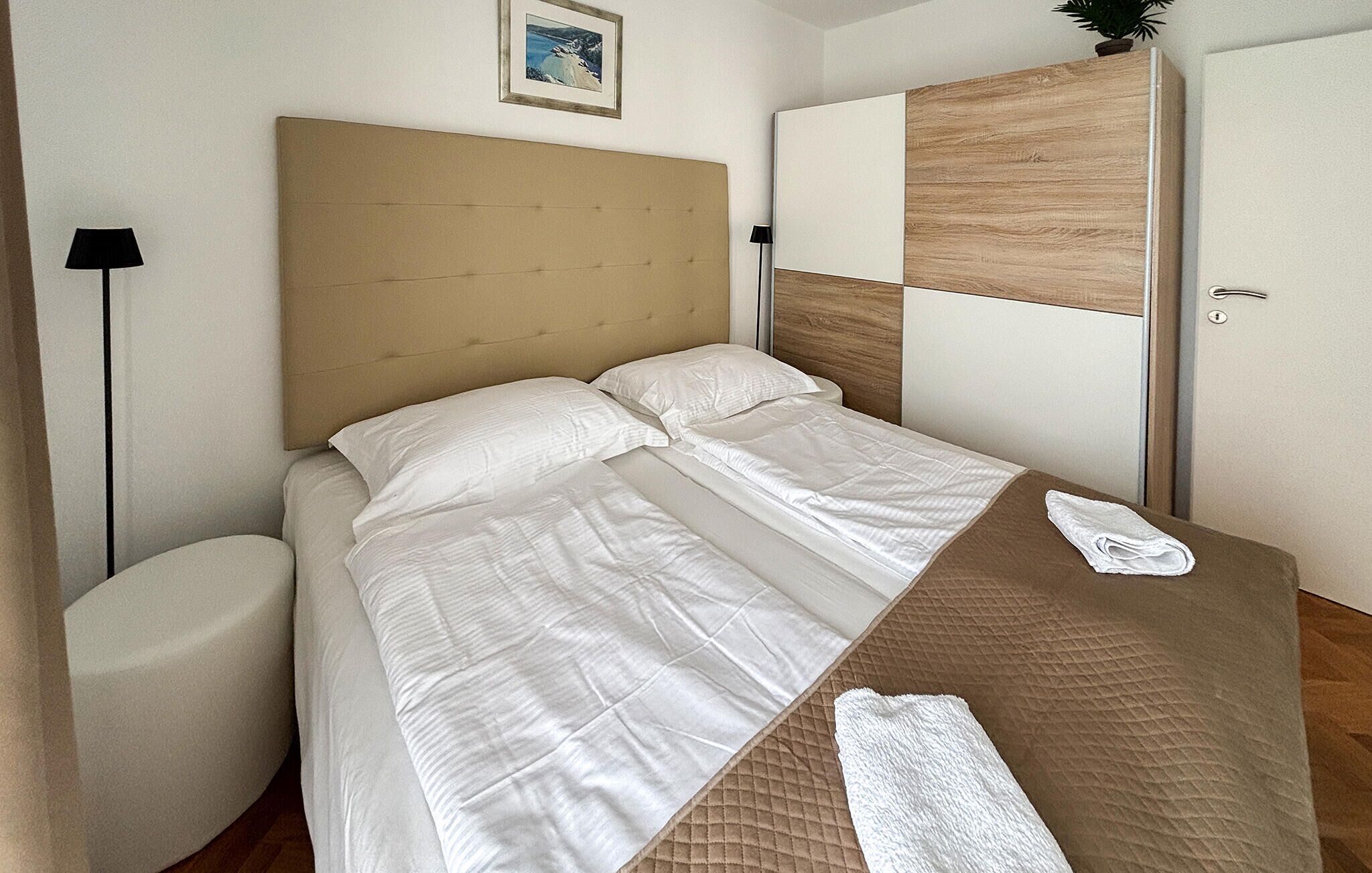 Een netjes opgemaakt bed met witte lakens, een houten hoofdbord en een nachtkastje met een opgevouwen witte handdoek.