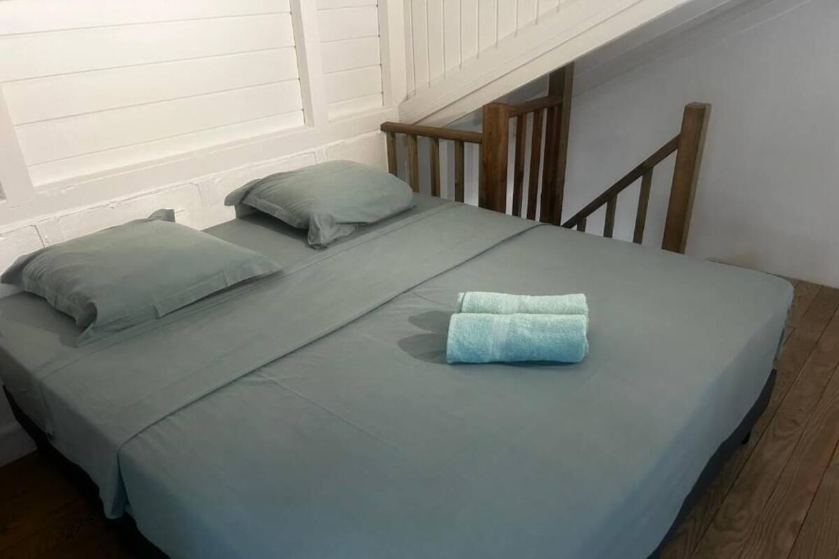 A single bed with a grey mattress and pillows, a wooden headboard, and a wooden staircase.