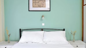 Un lit avec une literie blanche, deux tables de chevet ornées de vases, un tableau encadré au-dessus du lit et un interrupteur sur le mur.