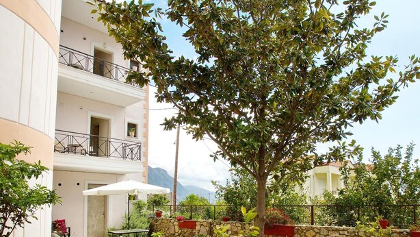 Une cour intérieure avec un mur en pierre, un arbre et un bâtiment blanc doté de balcons.