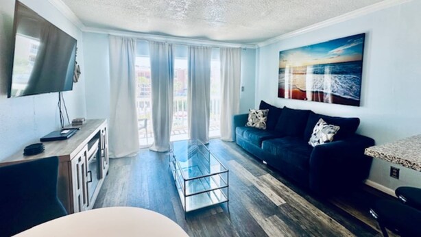 A modern living room with a flat-screen TV, a dark sofa, a glass coffee table, and a painting on the wall. - Sandy Seawall Escape Resort (Galveston)