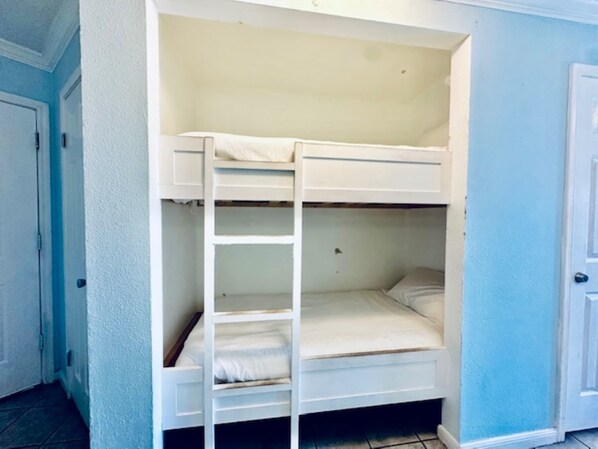 Een stapelbed met een ladder, witte muren en een deur.