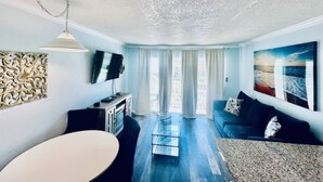 A living room with a sofa, a TV, a table, and a decorative wall piece. - Sandy Seawall Escape Resort (Galveston)