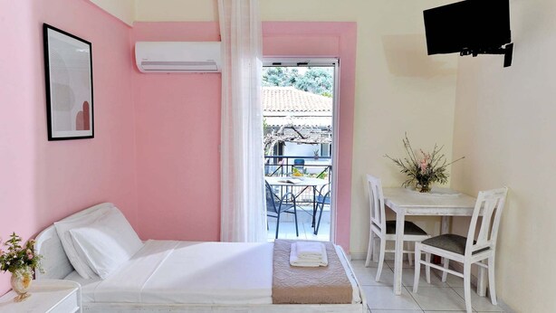 A bedroom with a bed, a desk, chairs, a TV, and a balcony with a table and chairs.