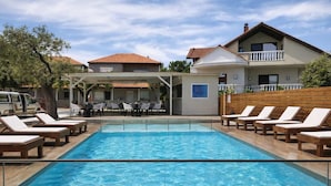 Une piscine avec des chaises longues, un espace extérieur aménagé et couvert, et un bâtiment doté d’un balcon.