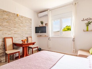 A bedroom with a bed, a desk with chairs, a TV, a window with curtains, and a brick wall. - Apartmani  STANIĆ - apt. A2 "Olive tree" by Interhome (Omiš)
