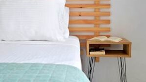 A bed with a wooden headboard, a white pillow, a teal blanket, and a nightstand with an open book. - Ilia Edipsos Superior Gem - Quaint and Cozy (Istiaia-Aidipsos)