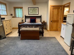 A bedroom with a bed, a wooden bench, a dresser, a desk, a lamp, a map on the wall, and a refrigerator.