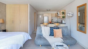 Ett kompakt bostadsutrymme med en säng, soffa, litet kök och en spegel.