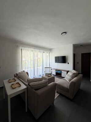 A modern living room with a sofa, a small table, and a TV mounted on the wall. - Playa Encuentro, located on the highest hill, a paradise surrounded by CAYENA flowers. (Puerto Plata)
