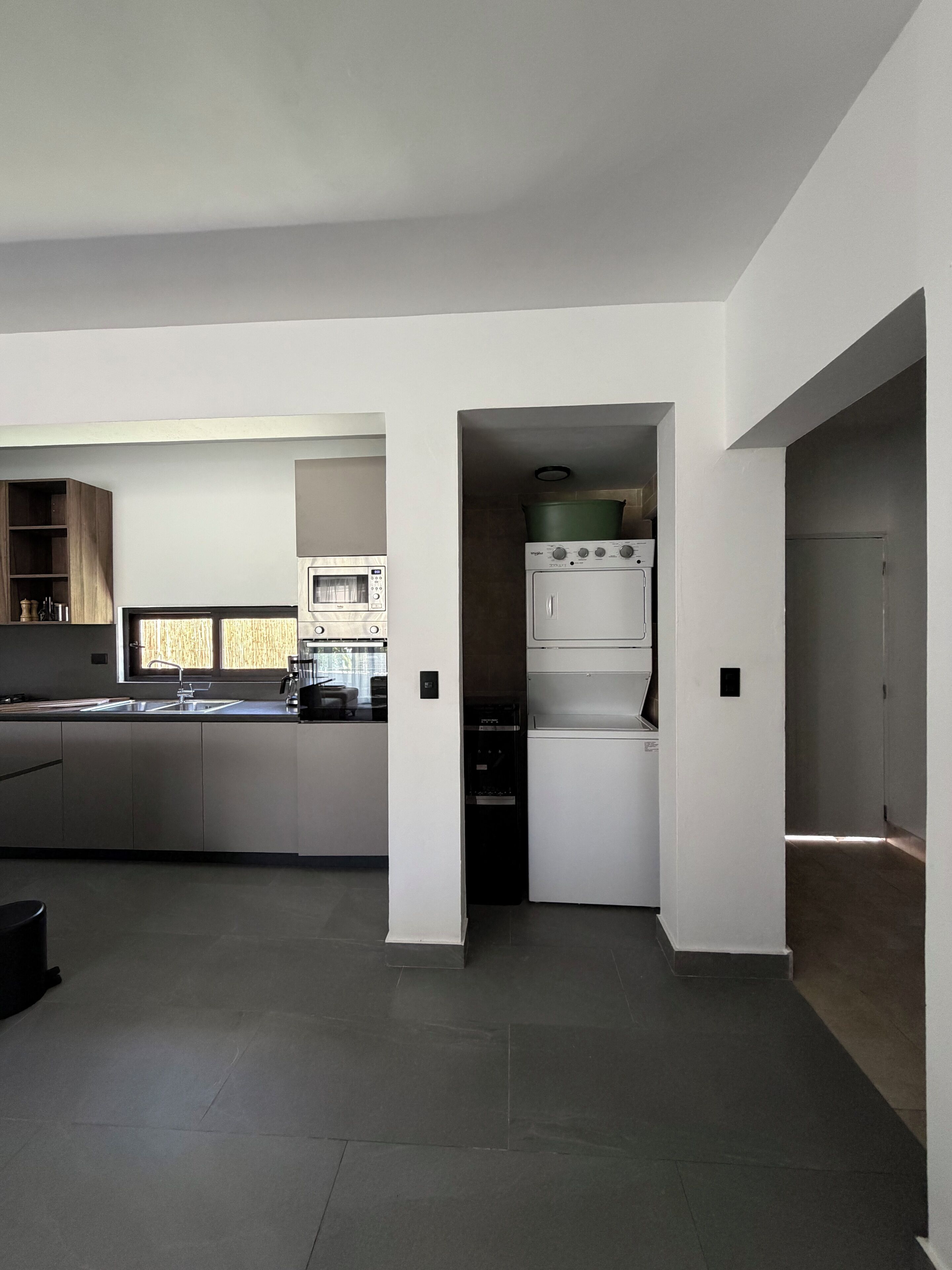 Una cucina moderna con forno a incasso e microonde, un'ampia finestra e un pavimento piastrellato scuro.