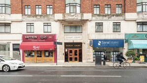 A street view with a building featuring a restaurant named 'Saffron,' a 'Dudley Court' entrance, and a 'SanaEstates' real estate office. - Central London Apartment 1BR - 5 Min to Hyde Park (London)