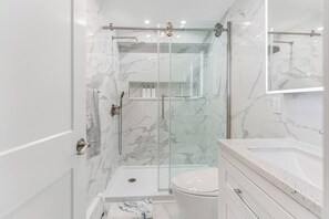 Et moderne badeværelse med en glasafskærmet brusekabine, toilet og et vaskeskab med spejl.