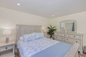 A bedroom with a bed, nightstands, a dresser, a mirror, and a potted plant.
